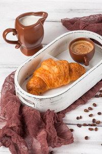 新鲜出炉的牛角面包, 在棕色的餐巾, 奶油, 在白色木制背景的陶瓷菜肴杯咖啡。早餐的新鲜糕点。美味的甜点特写摄影。垂直横幅