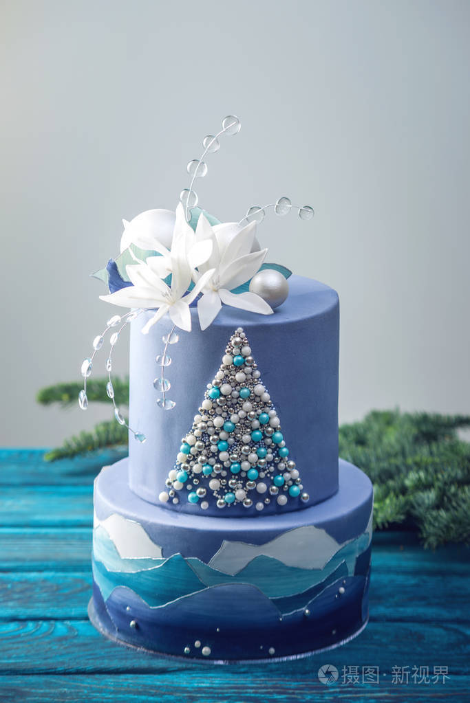 分层蛋糕的蓝色蛋糕与圣诞树和白色的花朵在上面的形象节日甜点的概念