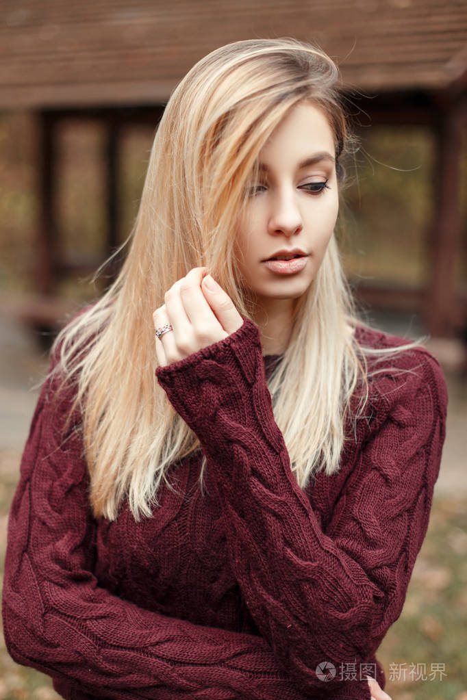 美丽的年轻的金发女郎在时尚针织复古毛衣在公园的自然