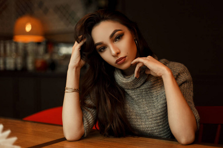 美丽的年轻女孩模型在一个时髦的针织毛衣坐在餐厅