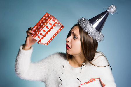 悲伤的年轻女孩在一个喜庆的帽子持有一个空的礼品盒, 她没有一个礼物