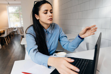 疲惫的年轻的黑发女孩自由职业者在咖啡馆努力工作笔记本电脑