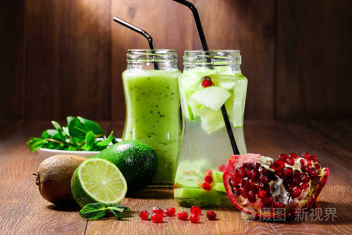 绿色鸡尾酒在一个玻璃罐子的猕猴桃, 绿色苹果, 薄荷, 石灰和石榴在一个木褐色背景。提神饮料。健康饮食排毒的概念
