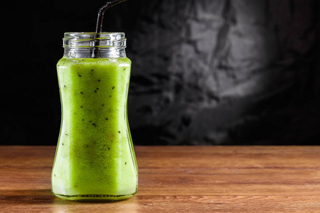 冰沙放在一个玻璃罐子里，里面是猕猴桃绿色苹果石灰薄荷和鳄梨，放在一张木桌上。 健康饮食排毒的概念。
