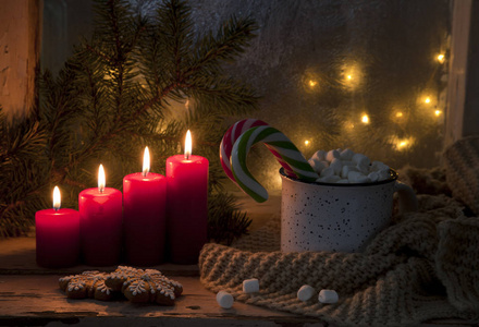在节日背景上，用棉花糖和带有红色蜡烛的圣诞装饰的糖果罐关闭热杯子。 圣诞概念。