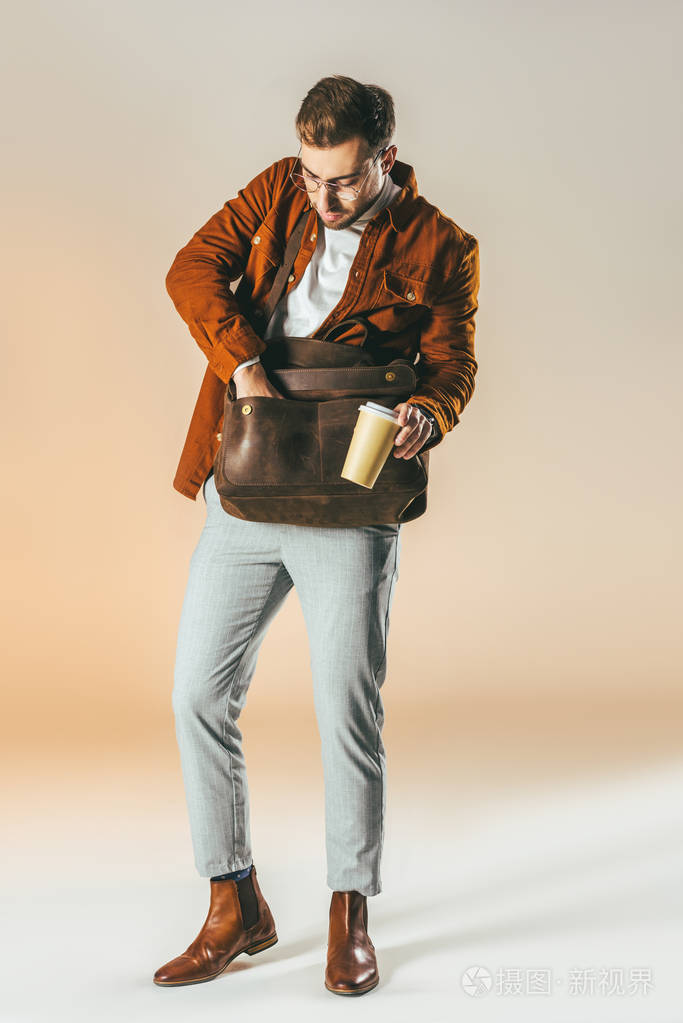 时尚男人带着咖啡手拿着在袋子里找东西
