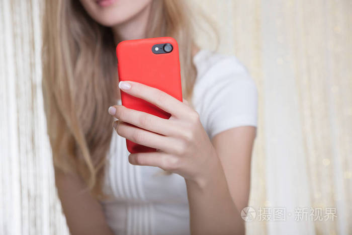 可爱的年轻女子穿着白色连衣裙,手里拿着红色的手机,自拍拍摄