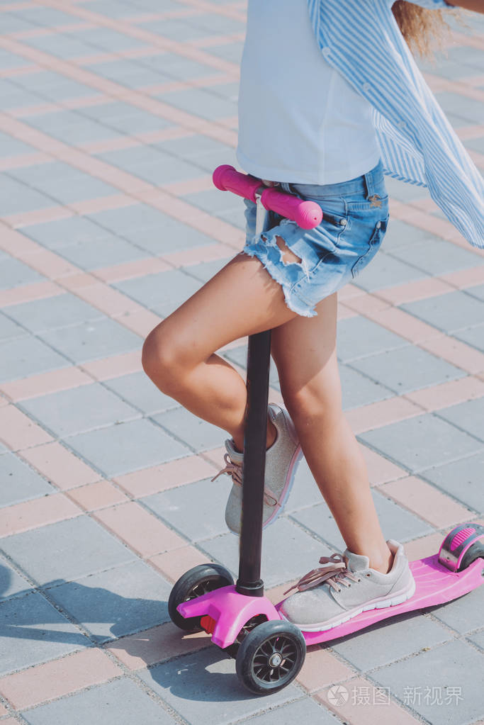 阳光明媚的一天小女孩骑着滑板车在街上