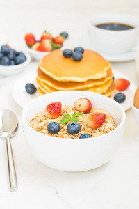 健康早餐套餐，包括煎饼和麦片蓝莓草莓和黑咖啡牛奶和橙汁，背景白石桌