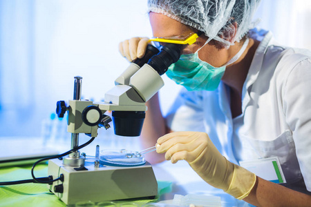 戴口罩的妇女在实验室用显微镜工作