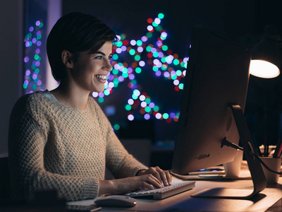 快乐微笑的年轻女子深夜与电脑连接，她在网上与朋友聊天和社交