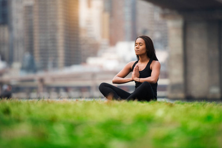 漂亮的非裔美国女人在纽约公园的绿草上缝补瑜伽