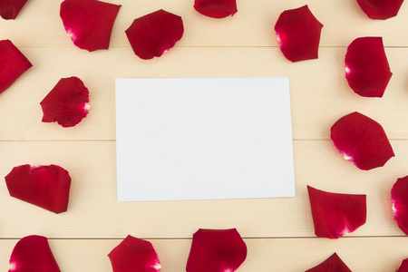 浅棕色木质背景下的红色玫瑰花瓣白色空白卡片