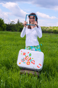 快乐的女孩站在绿色的草地上画的手提箱