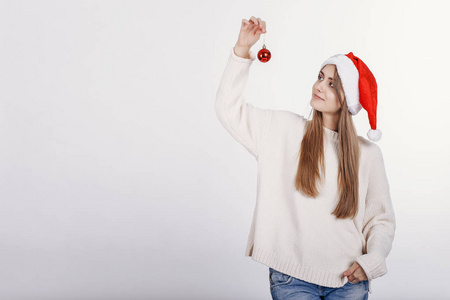 戴着圣诞帽的漂亮金发女郎手里拿着一个小小的圣诞球，看着它