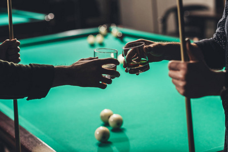 在酒吧台球桌前，用暗示和带酒精的眼镜拍摄男性双手的图像
