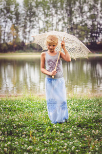 微笑的快乐女孩，带着白色的伞在大自然的河边