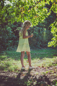 夏天，美丽的白种人女孩，一头金色的长发，穿着黄色的裙子，站在树下