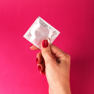 在粉红色背景下拿着避孕套的女人性保护概念