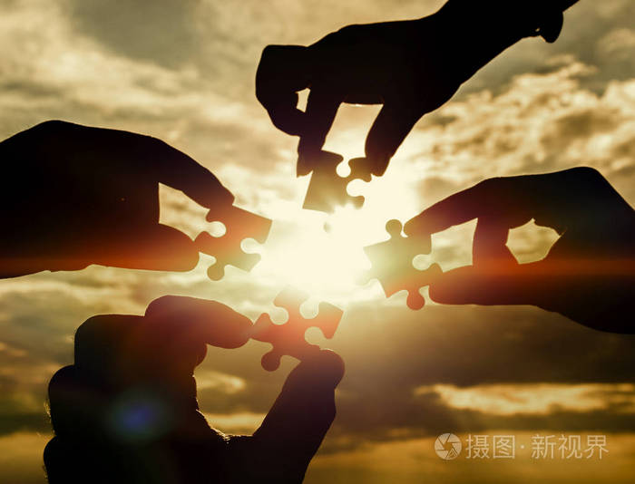 合作四只手试图连接一个拼图与日落背景. 一个拼图在手中对抗阳光.