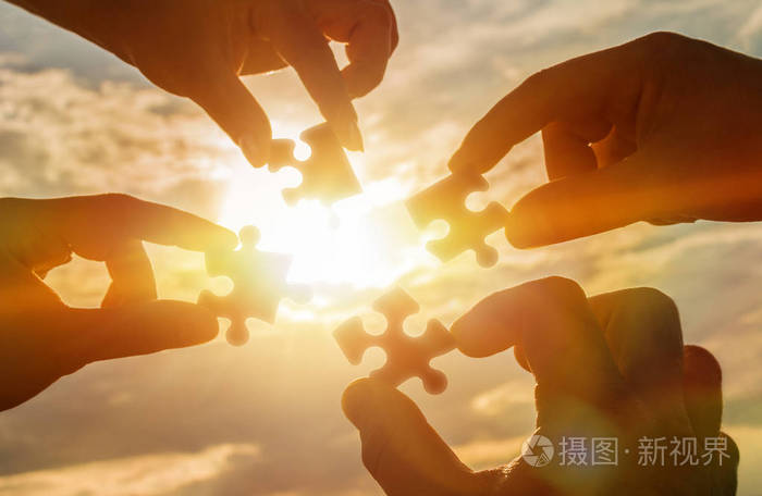 合作四只手试图连接一个拼图与日落背景. 一个拼图在手中对抗阳光.