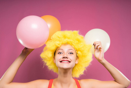 滑稽可笑的年轻女孩, 她的头上戴着滑稽黄色的假发, 手里拿着五彩的气球
