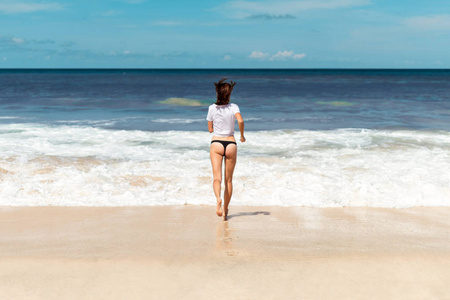 运动和健康的年轻女子在热带海滩上运行在日落期间比基尼泳装。印度尼西亚巴厘岛