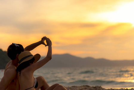 情侣相爱，在度假的日落海滩上用手在热带做一个心形。 蜜月在夏季旅游目的地一起放松。 情人节旅行和夏季概念