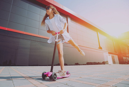 小女孩骑着滑板车在街上穿着白色连衣裙和帽子的年轻少女