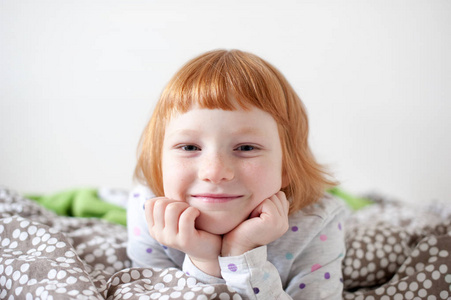 一个红头发的微笑女孩在床上的肖像