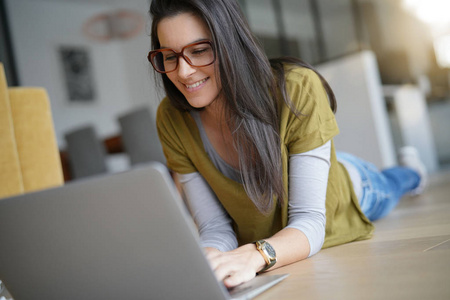 黑发女人躺在互联网上，用笔记本电脑连接地板