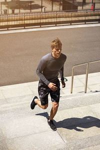 男运动员跑上楼梯的速度，运动的年轻人在运动的t恤训练或户外工作，而慢跑的台阶，耀斑的太阳