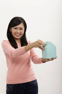 女人在白色背景上拿着一个房子形状的硬币盒子