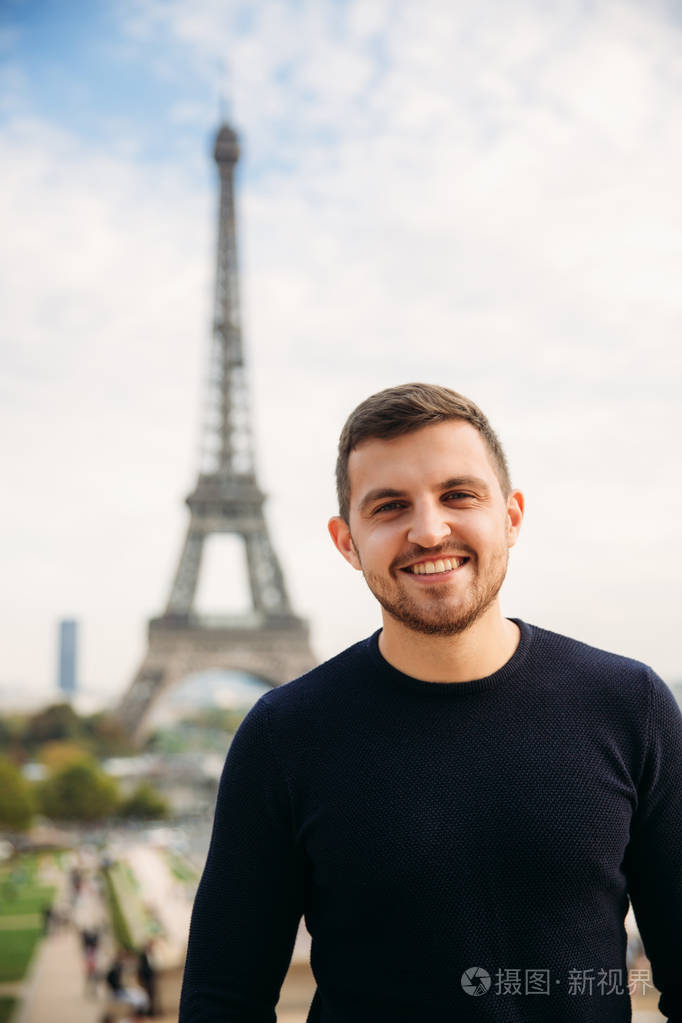 一个身穿深蓝色夹克的年轻人站在埃菲尔铁塔的背景上晴朗的天气是秋天