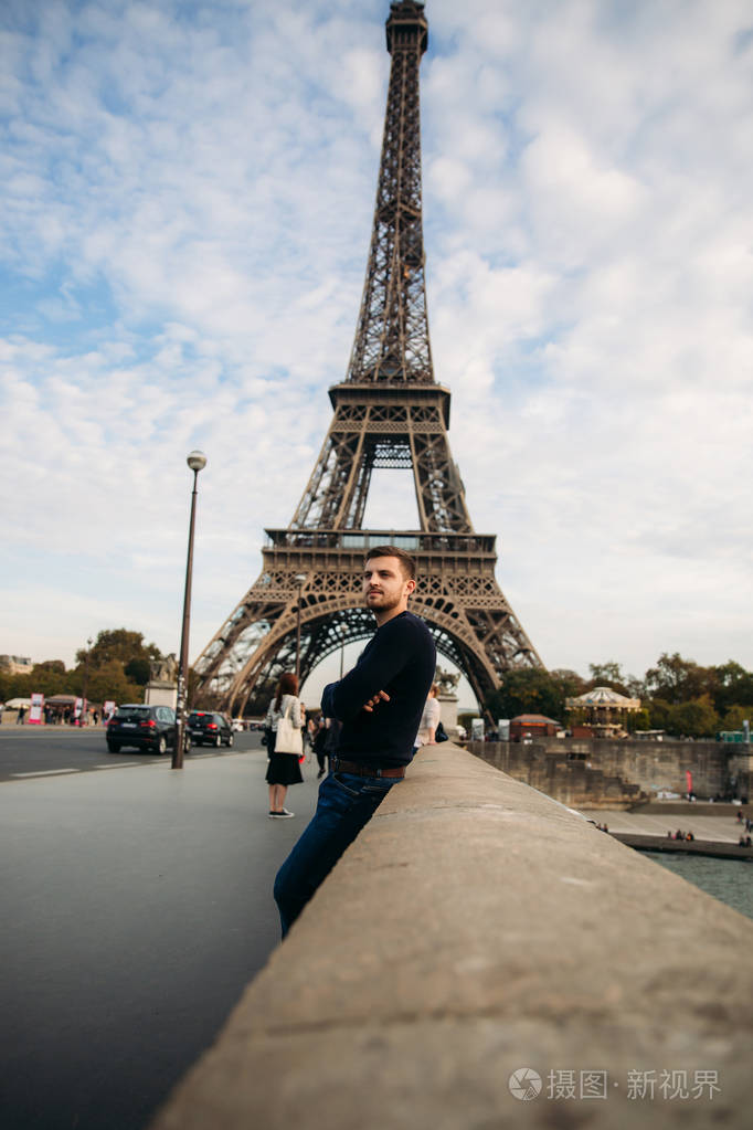 一个身穿深蓝色夹克的年轻人站在埃菲尔铁塔的背景上晴朗的天气是秋天