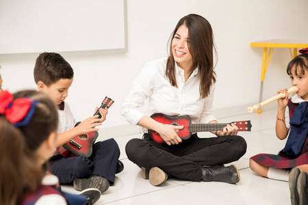 有趣的女幼儿教师弹吉他，教她的学生一些音乐