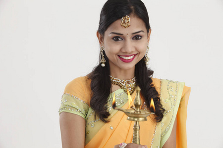 美丽的年轻印度妇女，穿着传统的莎莉服装，手持一盏排灯油灯，隔离在白色背景上。