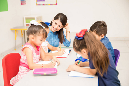 快乐幼儿园女老师在课堂上帮助她的学生做一些写作练习