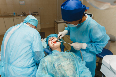 男老专业牙医医生在制服和女助手帮助执行操作安装妇女患者的牙种植牙在诊所轻的办公室与现代工具设备