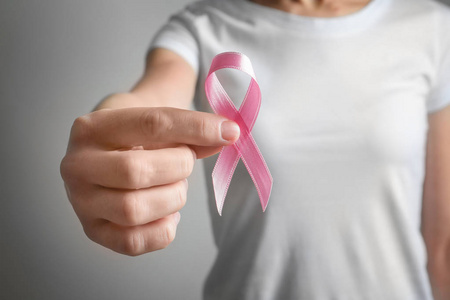 在灰色背景下手持粉红色缎带的妇女。乳癌意识概念