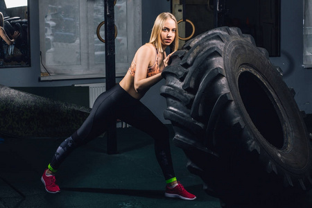 适合女性运动员与一个巨大的轮胎工作, 在健身房翻转