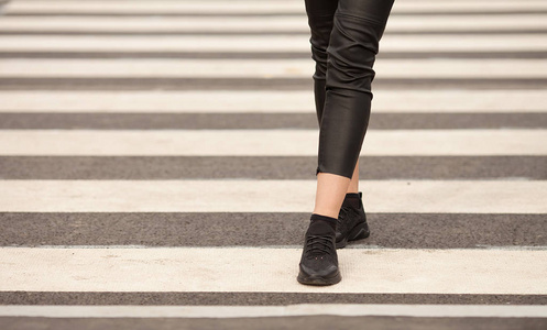 合上走在人行横道上的女人腿。 那个女人穿着黑色运动鞋。