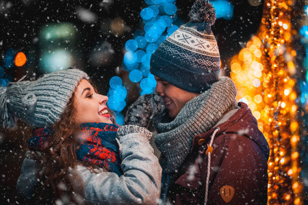 爱的情侣在圣诞灯的背景晚上漫步在城市与降雪