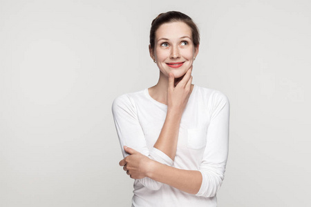 困惑的年轻成年美女拥抱自己摸下巴,抬头看.