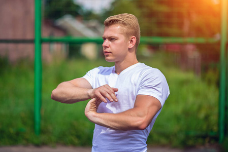 一个男运动员在露天参加体育运动。肌肉手臂。穿着白色 t恤衫的金发女郎健美运动员的生活方式