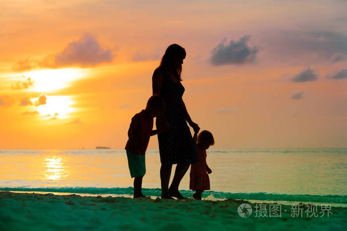 母亲和两个孩子在日落时在海滩上行走