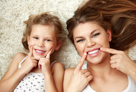 美丽女儿的肖像，妈妈展示了他们健康的白色微笑，躺在家里的地毯上。