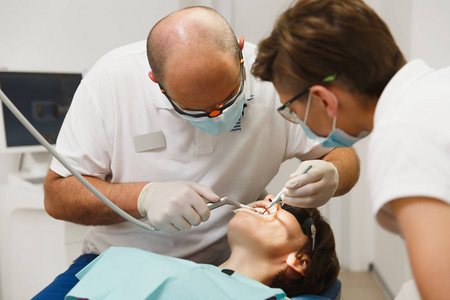 牙科陶瓷冠的制备和安装过程。男性专业牙医和女助手帮助治疗女性患者的牙齿在诊所光办公室与现代工具设备