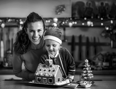 微笑的母亲和婴儿在厨房装饰圣诞饼干屋