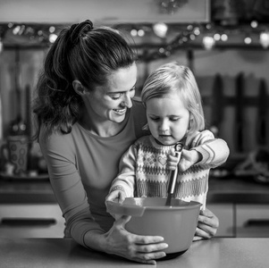 快乐的母亲和婴儿在圣诞节装饰的厨房里搅拌面团